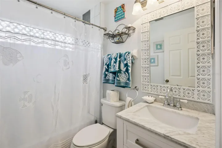 Updated guest bathroom with vanity, decorative mirror, shower and tub combination, and coastal style accents.