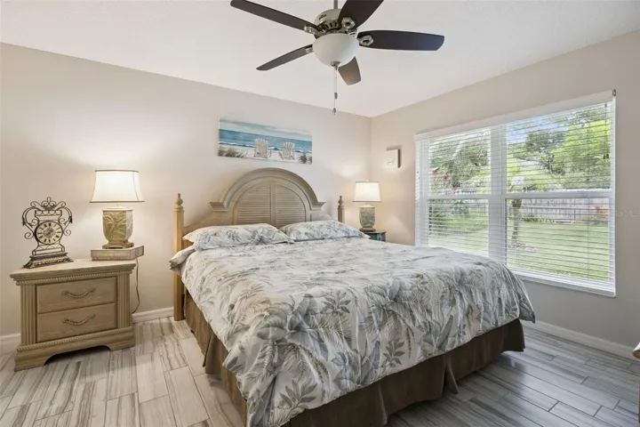 Primary bedroom with updated tile flooring, ceiling fan, neutral tones, and a large window overlooking the backyard