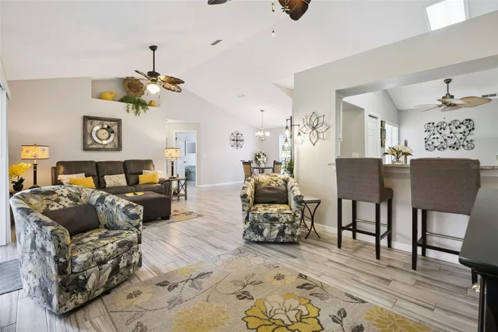 Open concept living space with vaulted ceilings, updated flooring, breakfast bar seating, and easy flow into the updated kitchen and dining areas.