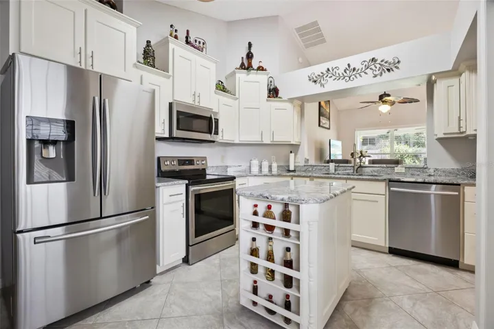 Updated kitchen in this Eustis home featuring granite countertops, stainless steel appliances, white cabinetry, center island, and abundant storage.