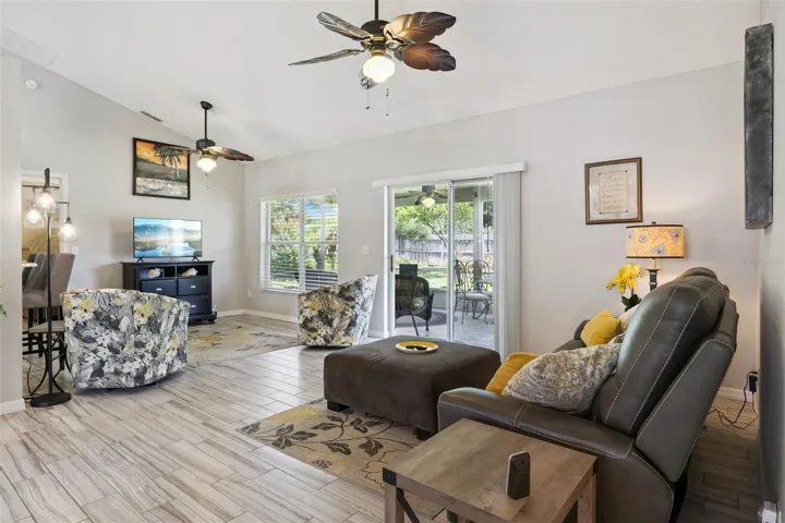 Open living room with vaulted ceilings, updated tile flooring, large windows, and sliding glass doors leading to the screened patio and fenced backyard.