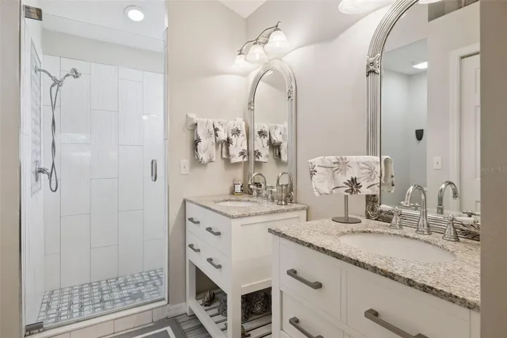 Updated en suite bathroom featuring dual vanities, granite counters, modern fixtures, and a walk in shower.