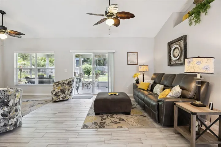 Comfortable living area with vaulted ceiling, large window, updated tile flooring, and direct access to the screened back patio.