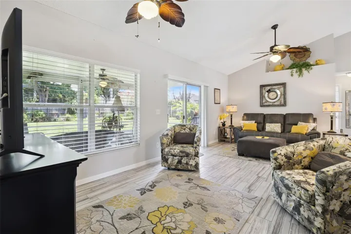 Spacious living room with open sightlines, vaulted ceiling, updated flooring, and connection to the kitchen and dining areas.