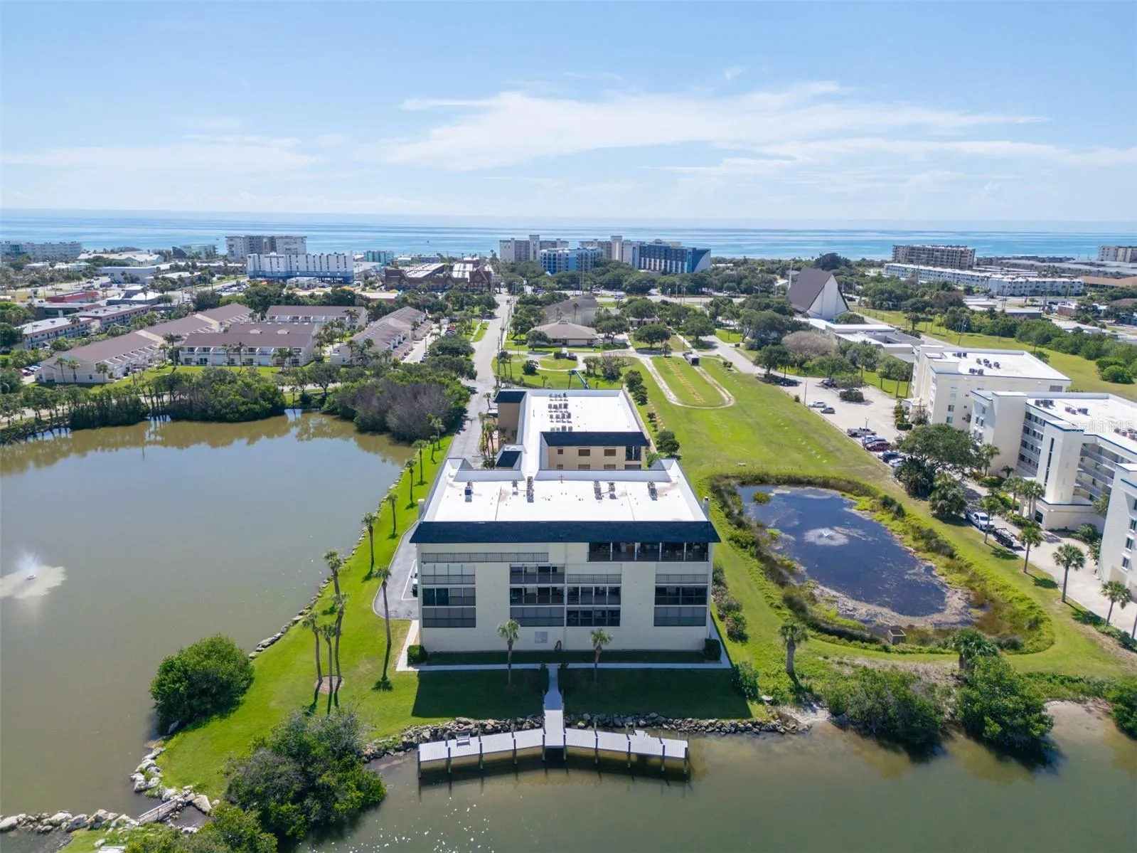 Aerial view of Riverwest condominium property with pond, fishing dock, and ocean view in the distance