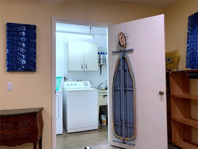 Interior laundry room with utility sink, iron and ironing board. Water heather and electrical panel are also in the laundry room. Cleaning supplies in the cabinet on the wall.