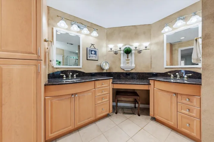 Primary bathroom with double vanities, wood cabinets, granite counters