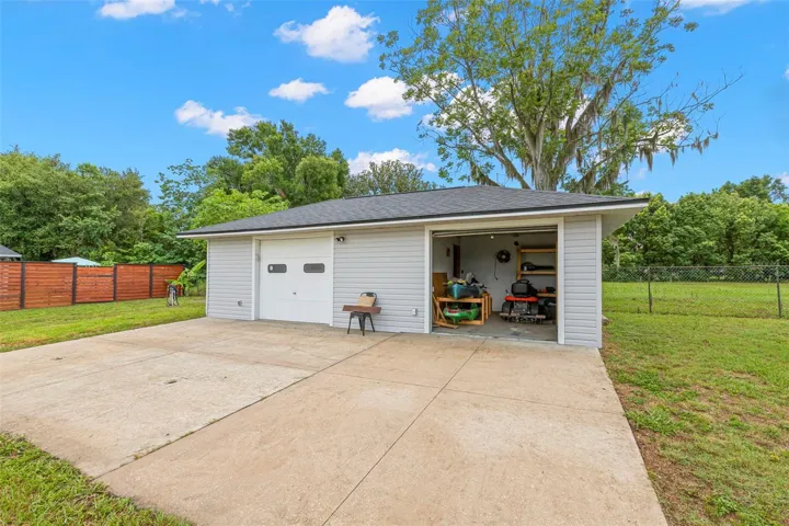 View of separated 1 car garage room within the detached over-sized 2 car garage and riding mower conveys with sale.