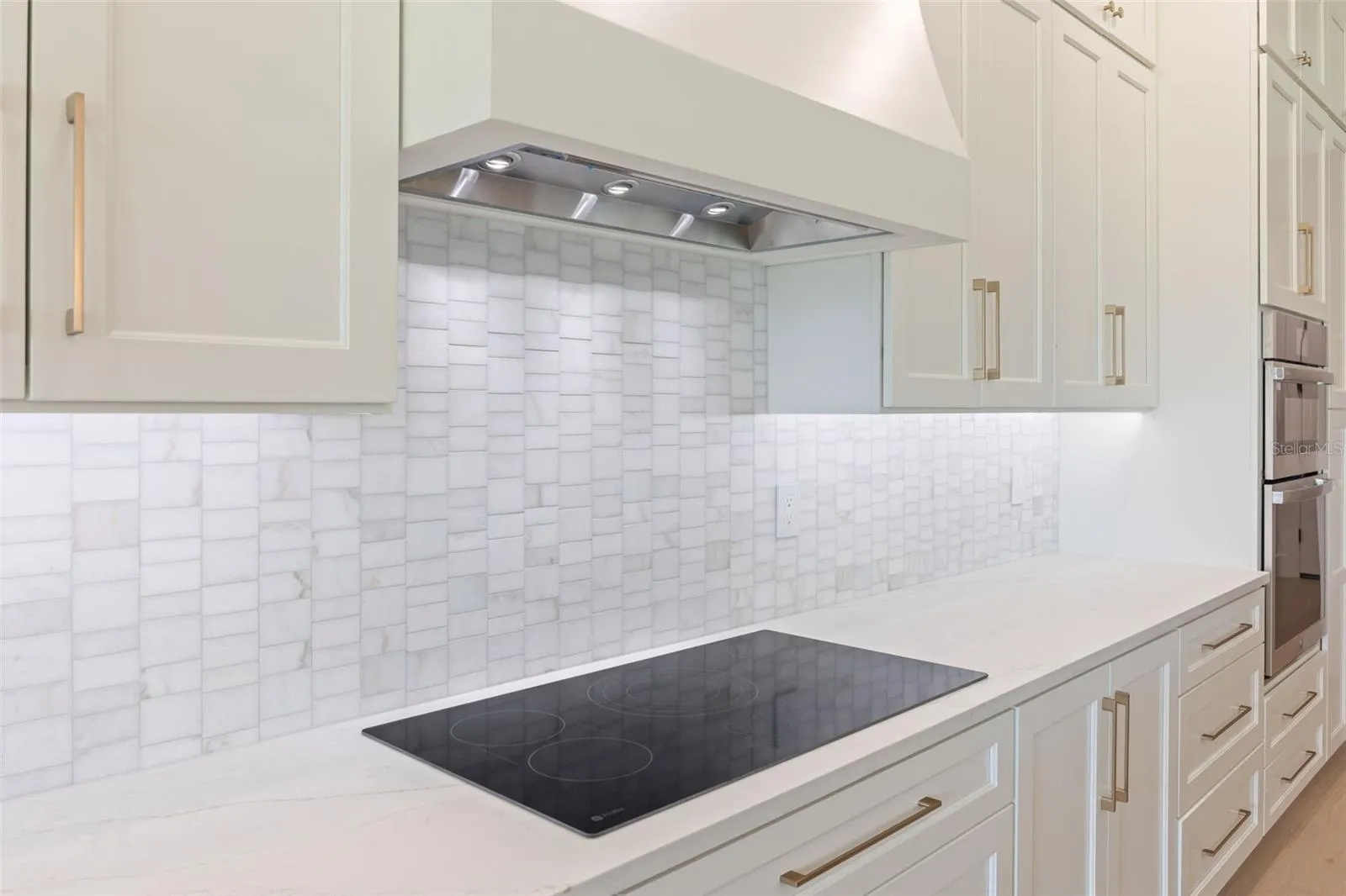 The gourmet kitchen is a true showpiece, featuring full-height custom cabinetry, an oversized 11-foot quartz island with storage on both sides, marble backsplash, GE Profile appliances, custom range hood, cooktop, wall oven, and soft-close cabinetry throughout.