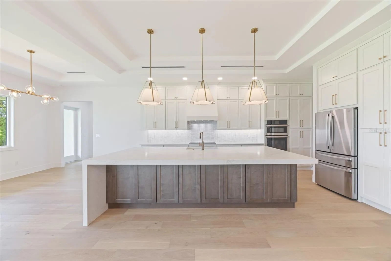 The gourmet kitchen is a true showpiece, featuring full-height custom cabinetry, an oversized 11-foot quartz island with storage on both sides, marble backsplash, GE Profile appliances, custom range hood, cooktop, wall oven, and soft-close cabinetry throughout.