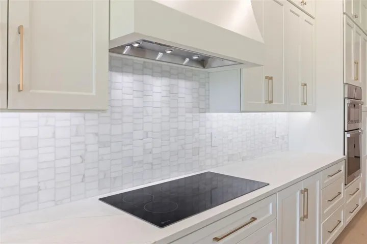 The gourmet kitchen is a true showpiece, featuring full-height custom cabinetry, an oversized 11-foot quartz island with storage on both sides, marble backsplash, GE Profile appliances, custom range hood, cooktop, wall oven, and soft-close cabinetry throughout.