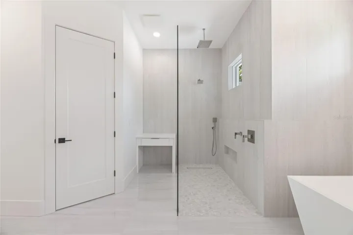 The luxurious primary suite offers a spa-inspired retreat featuring a freestanding soaking tub, oversized walk-in shower with rain head and handheld shower, premium Italian tile, designer fixtures, and thoughtful custom details throughout.