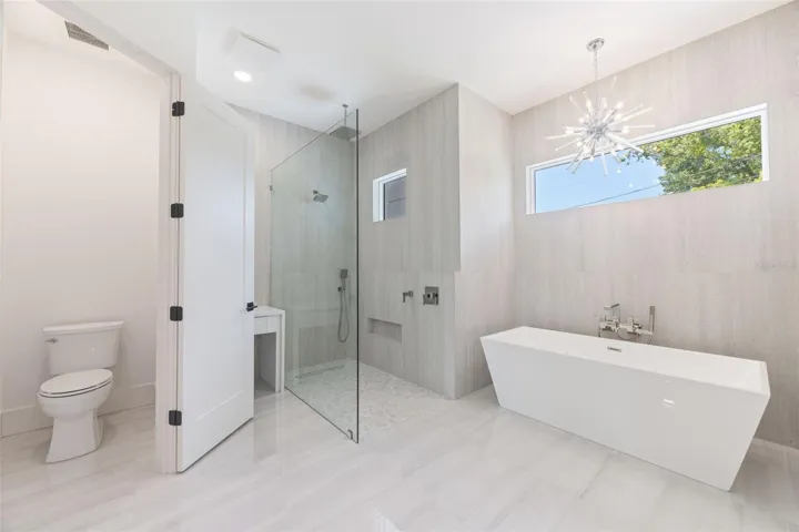 The luxurious primary suite offers a spa-inspired retreat featuring a freestanding soaking tub, oversized walk-in shower with rain head and handheld shower, premium Italian tile, designer fixtures, and thoughtful custom details throughout.