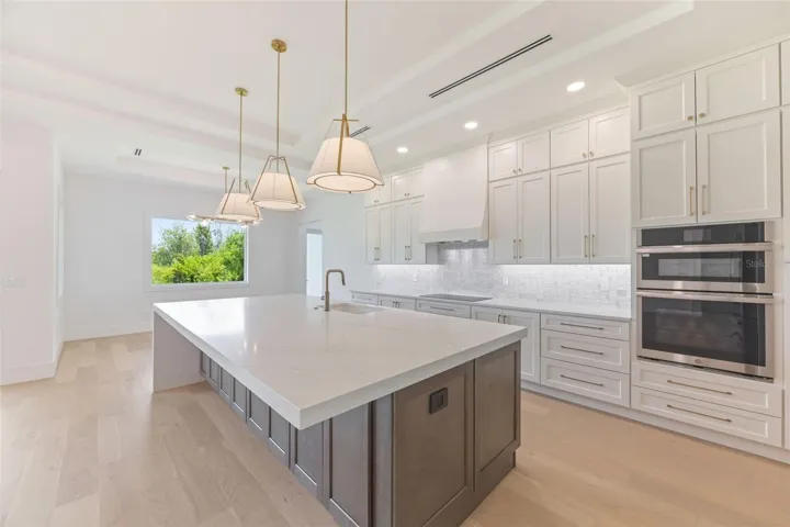 The gourmet kitchen is a true showpiece, featuring full-height custom cabinetry, an oversized 11-foot quartz island with storage on both sides, marble backsplash, GE Profile appliances, custom range hood, cooktop, wall oven, and soft-close cabinetry throughout.