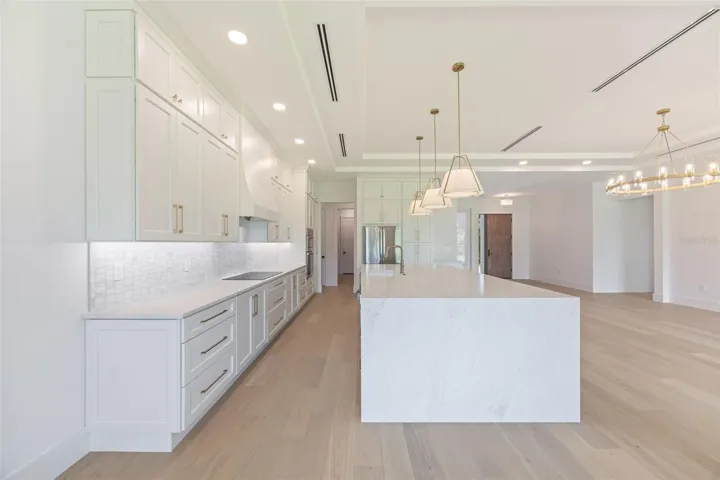 The gourmet kitchen is a true showpiece, featuring full-height custom cabinetry, an oversized 11-foot quartz island with storage on both sides, marble backsplash, GE Profile appliances, custom range hood, cooktop, wall oven, and soft-close cabinetry throughout.