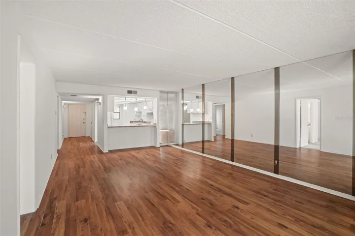 Spacious from Every Angle. The open living and dining areas are anchored by warm laminate flooring, a breakfast bar with pendant lighting, and a mirrored wall that enhances the room.