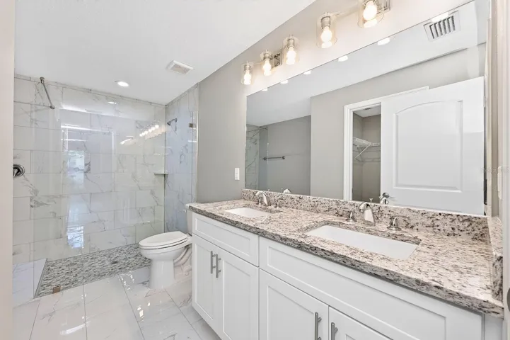 The Primary EN SUITE BATH is complete with dual sinks, stone countertops, and a stunning OVERSIZED GLASS-ENCLOSED TILED SHOWER.
