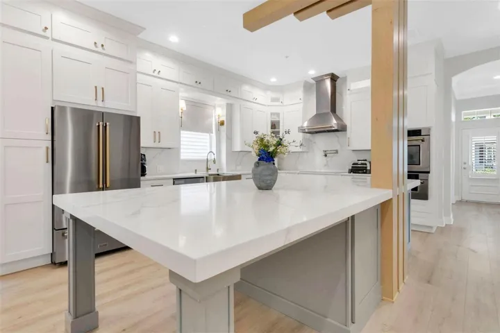 Bright white, ceiling-height shaker perimeter cabinetry maximizes storage and features contemporary gold hardware, seamlessly framing a large French-door stainless steel refrigerator