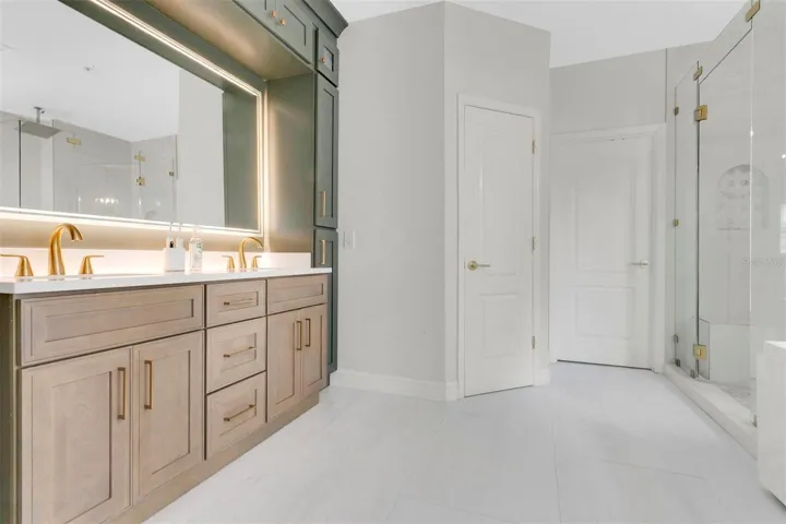 Spa-like bathroom boasts a two-tone vanity with floor-to-ceiling cabinets, a relaxing spa tub, a frameless glass shower, and subtle gray tilework that contrasts beautifully against dark green and light wood cabinetry