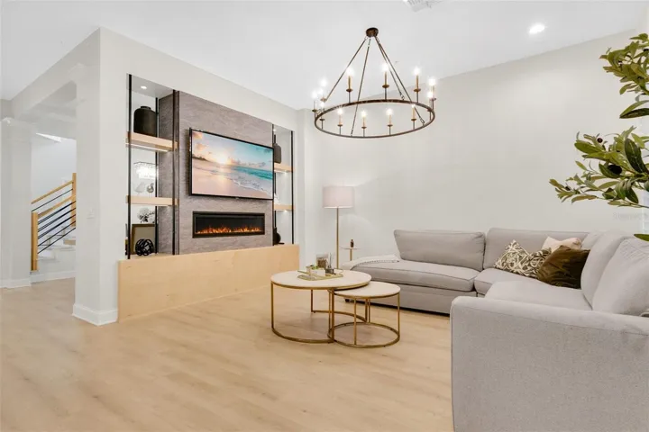 A modern entertainment wall separates these living spaces, showcasing a textured gray center panel, a wall-mounted television, and a linear electric fireplace flanked by custom open shelving on a light wood base