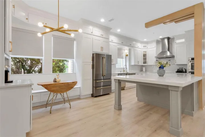 High-end culinary details include a custom white cabinet tower with flush-recessed luxury ZLINE appliances, a professional induction cooktop beneath a chimney-style range hood, and a dual-jointed bronze pot filler mounted on a full-height marble slab backsplash