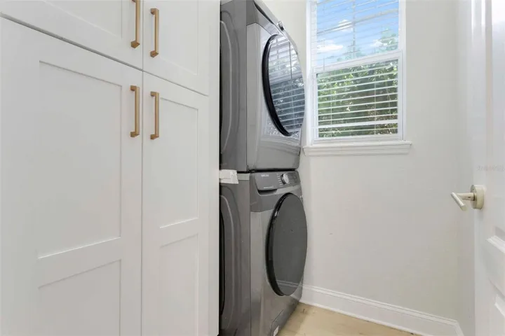 Reconfigured laundry room equipped with a stacked, front-loading washer and dryer alongside floor-to-ceiling white shaker cabinets