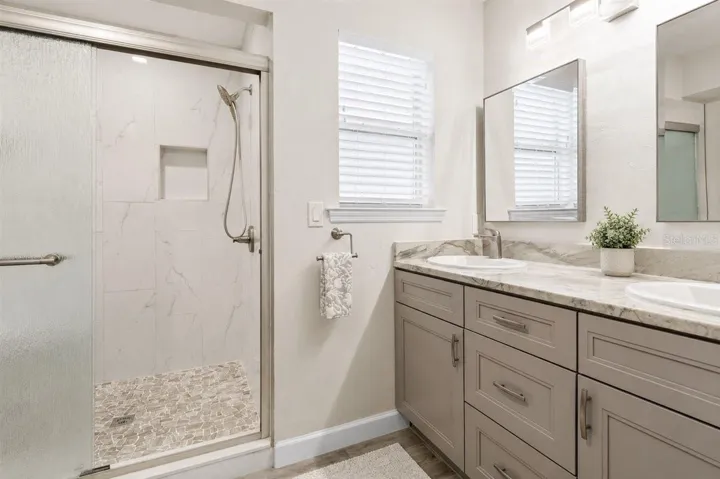 Beautifully updated luxury primary bathroom with stone counters and double-sink vanity.