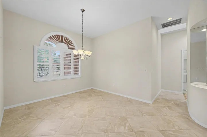 Formal dining room, highlighting its neutral color palette and spacious layout. The room features plantation shutters, abundant natural light, and detailed baseboards, showcasing the quality finishes and versatile use of the space.