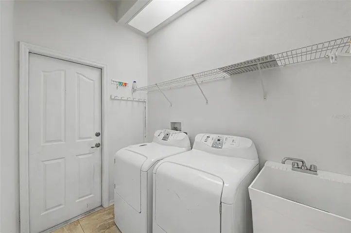 Fully functional laundry room equipped with a washer and dryer, both included with the home. The space also features a utility sink, overhead hanging rack for air-drying garments, and ample room for everyday laundry tasks, combining convenience with practical functionality.