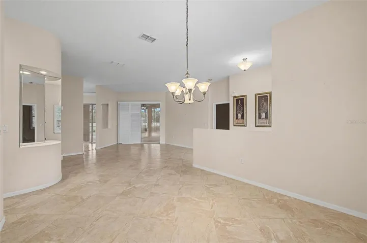 Dining area with a clear view into the formal sitting room, showcasing an open and connected floor plan. The space features a sliding glass door with plantation shutters, providing direct access to the pool area and bringing in abundant natural light. Neutral tones and quality finishes enhance the home’s seamless indoor-outdoor living experience.