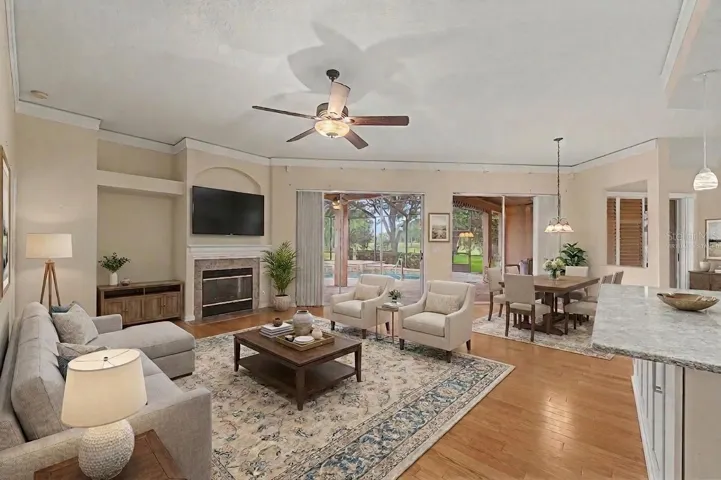 Main living room featuring a spacious, virtually staged layout with flexible areas for both seating and dining. The room showcases wood plank flooring, detailed baseboards, and a fireplace as a focal point. Two large sliding glass doors provide abundant natural light and open to views of the pool and a nearby golf course hole, enhancing the indoor-outdoor living experience.