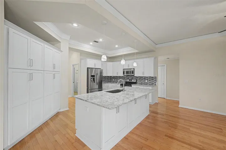 The oversized granite island serves as the heart of the kitchen, featuring built-in electrical outlets for convenient use of small appliances and device charging. Thoughtfully designed with cabinetry on both the working side and the seating side, the island provides exceptional storage while offering ample space for casual dining and entertaining. Complete with abundant cabinetry, a stylish tile backsplash, stainless steel appliances, recessed and pendant lighting, and generous counter space, this kitchen is as functional as it is beautiful.