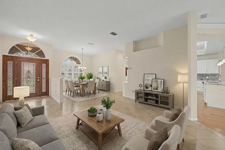 Stunning entryway featuring a beautiful wood front door that opens into a bright, open layout with neutral tones and large tile flooring throughout. Virtually staged formal dining room flows seamlessly into a well-designed sitting area, also virtually staged, showcasing the home’s versatile and inviting layout. The space highlights excellent natural light, tasteful finishes, and a welcoming, functional floor plan.