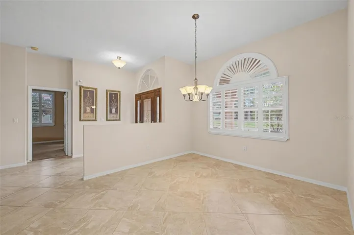 Front entry interior view showcasing the home’s welcoming foyer with a clear sightline into the formal dining room and the entrance to the master suite. The space features neutral tones, plantation shutters, and detailed baseboards, emphasizing the open flow and functional layout of the home.
