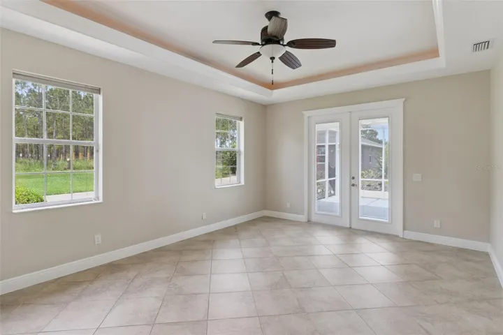 Primary Bedroom with tray ceiling and french doors leading out to screen porch