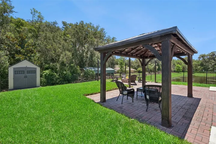Fire pit, gazebo,large paved patio facing pond on one side and partially wooded on the other side, storage shed for added convenience