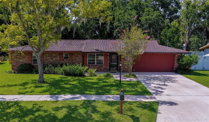 Charming ranch-style home featuring a spacious front yard, mature trees, and a wide concrete driveway leading to a two-car garage.