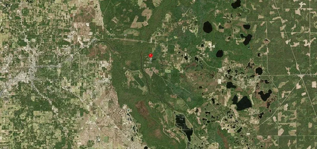 Large view aerial photograph showing location of property (red dot in center), City of Ocala to the left (west) and the wildlife management area and national forest with numerous lakes to the right (east).