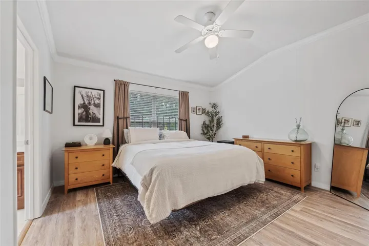 Primary bedroom featuring laminate flooring, ceiling fan, blinds, crown molding and ensuite bathroom