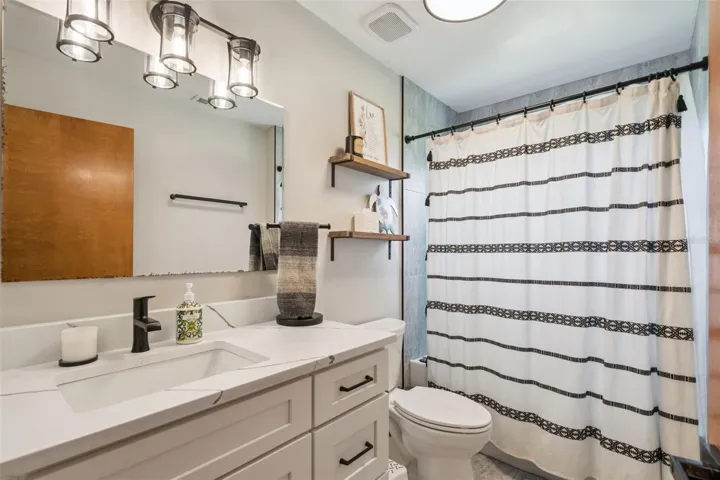 Updated guest bathroom with renovated vanity, shower area, flooring, and clean neutral finishes.