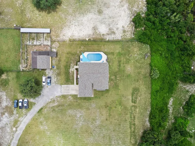 Overhead aerial of the pool, screened lanai, home, driveway, and property layout. Pool faces West, front of home faces East. Driveway and barn/workshop are to the South of the home.
