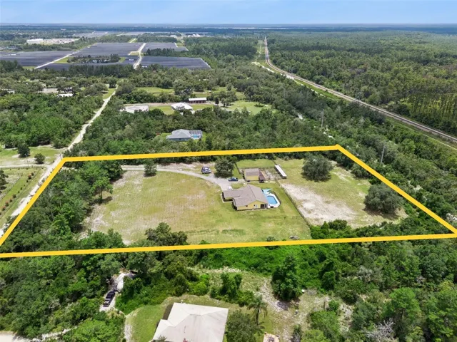 Aerial view showcasing the private 5 acre setting, home, barn, fenced land, and surrounding natural privacy.