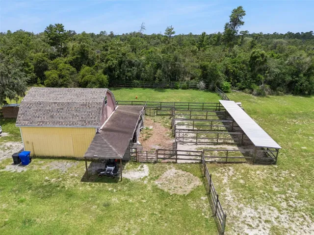 Aerial view of barn, fenced areas, and the property’s outdoor utility spaces.