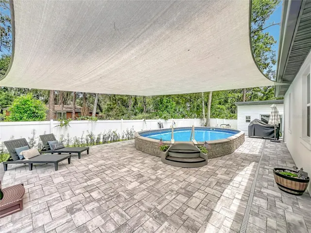 Semi above ground pool with pavers and sun shade.