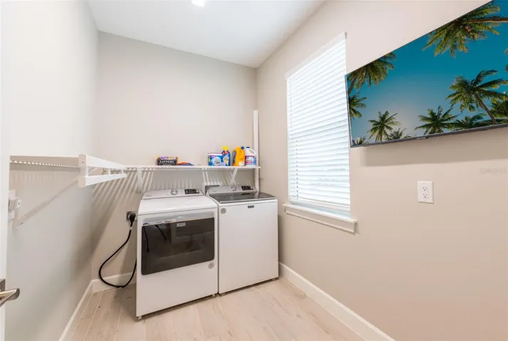 Laundry day made easy! The dedicated indoor utility room features high-efficiency washer and dryer units, built-in storage shelving, a bright window, and a wall-mounted TV setup—combining absolute functionality with modern convenience.
