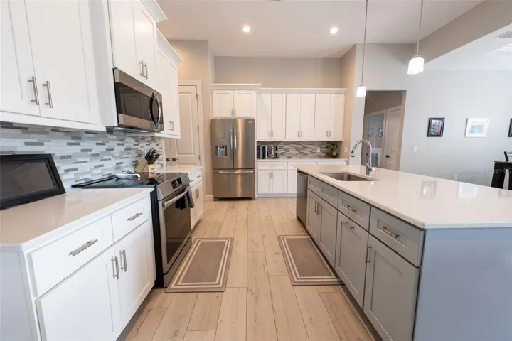 Pristine perspective of the kitchen showing the premium stainless steel range, undermount sink, and the contrast between the clean white perimeter cabinetry and the contrasting soft gray/blue island. Modern design meets everyday comfort in this Punta Gorda masterpiece.