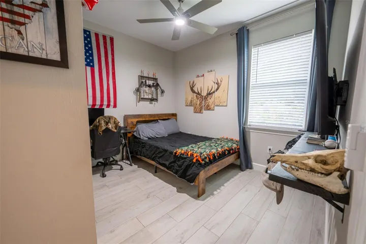 The spacious guest bedrooms in this split floor plan offer maximum privacy and style. Features include continuous wood-look porcelain tile flooring, high ceilings with modern paddle fans, a large window letting in beautiful natural light, and plenty of space for a full bedroom set and workstation.
