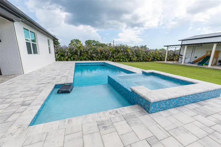 Dive into luxury! This close-up view of the spectacular custom swimming pool highlights the oversized sun shelf (baja shelf) perfect for lounging, a built-in raised spa with premium blue mosaic tile inlay, and a durable, expansive paver deck designed for low-maintenance outdoor living.