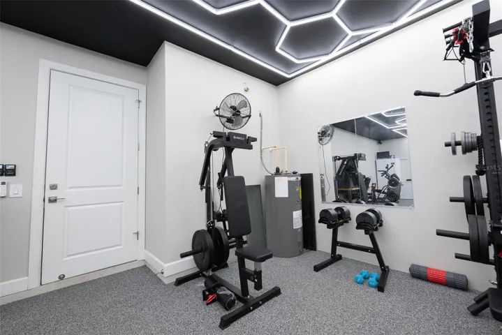 Another perspective of the ultimate attached home gym, highlighting a dedicated secondary workout zone. This conditioned space features commercial-grade flooring, bright white walls, and a large wall mirror, all illuminated by the premium custom hexagon LED grid ceiling lighting system.