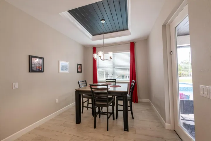 Host unforgettable dinners in the formal dining room, showcasing a beautiful recessed tray ceiling with dark wood paneling, a contemporary transitional chandelier, and high-end porcelain tile flooring. A glass door provides direct access to the outdoor living area.